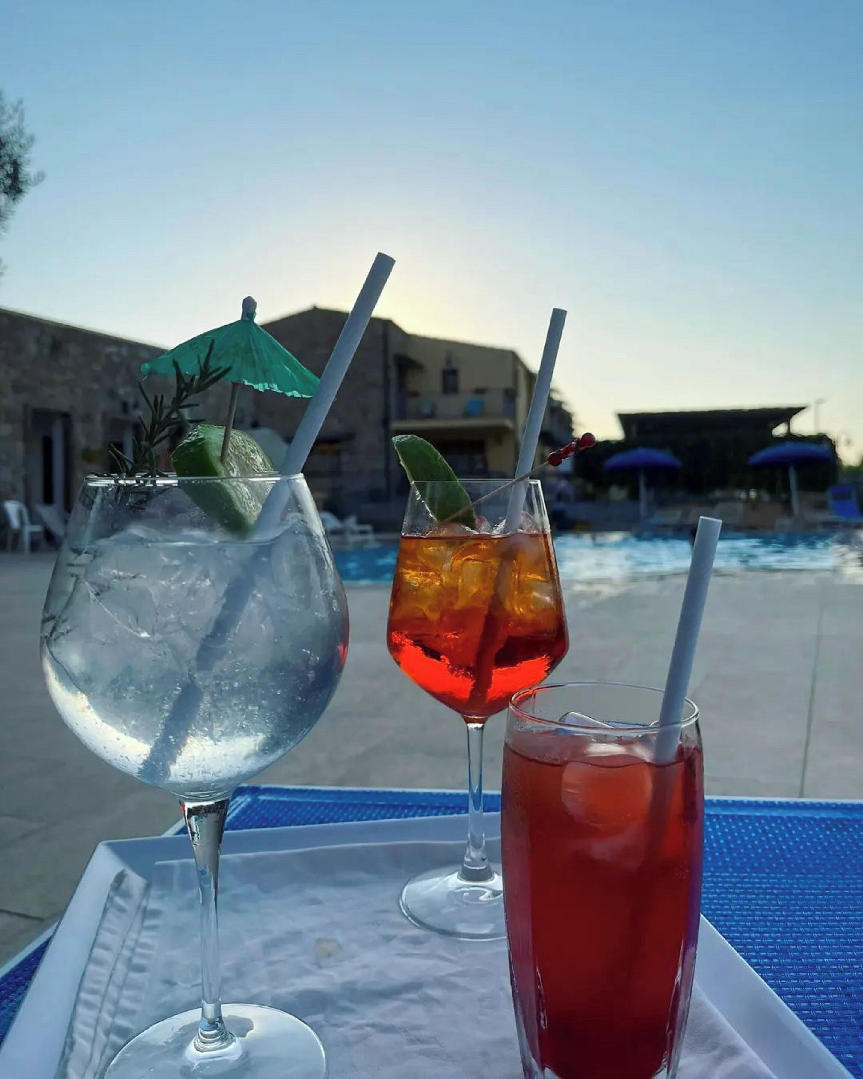 Tres bebidas sobre una bandeja junto a una piscina con un edificio al fondo.