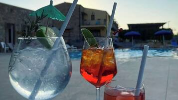Tres bebidas sobre una bandeja junto a una piscina con un edificio al fondo.