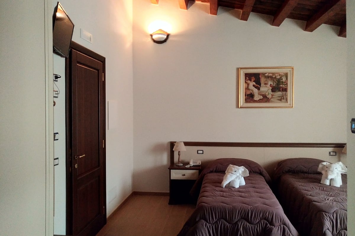 Una habitación de hotel con dos camas, un armario, una mesita de noche y una lámpara fijada a la pared.