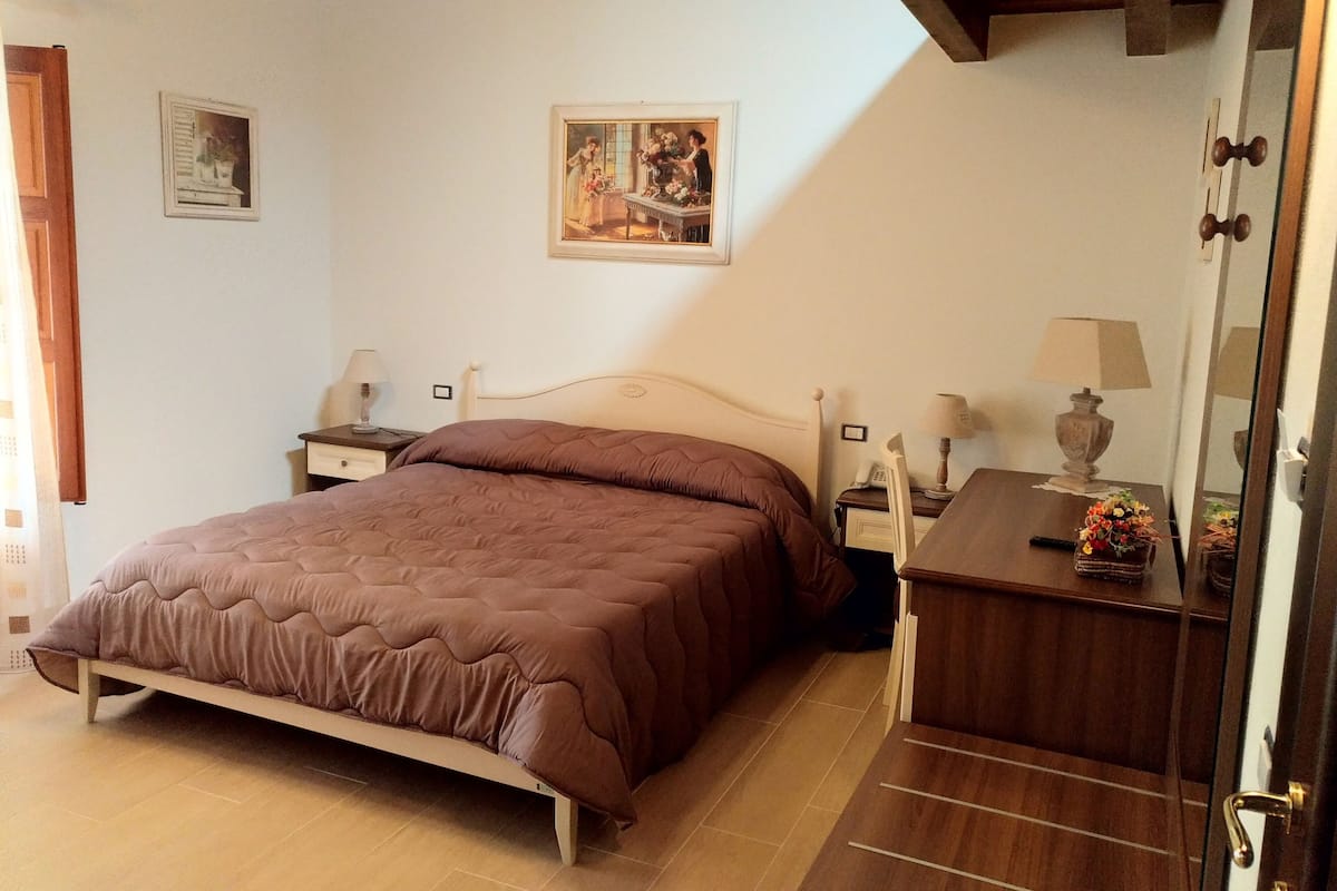 Un dormitorio con cama, mesitas de noche, espejo y un cuadro en la pared.