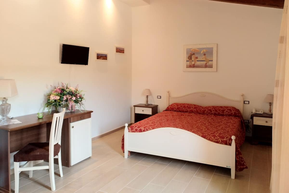 Un dormitorio con cama, escritorio, silla, televisor y un cuadro en la pared.