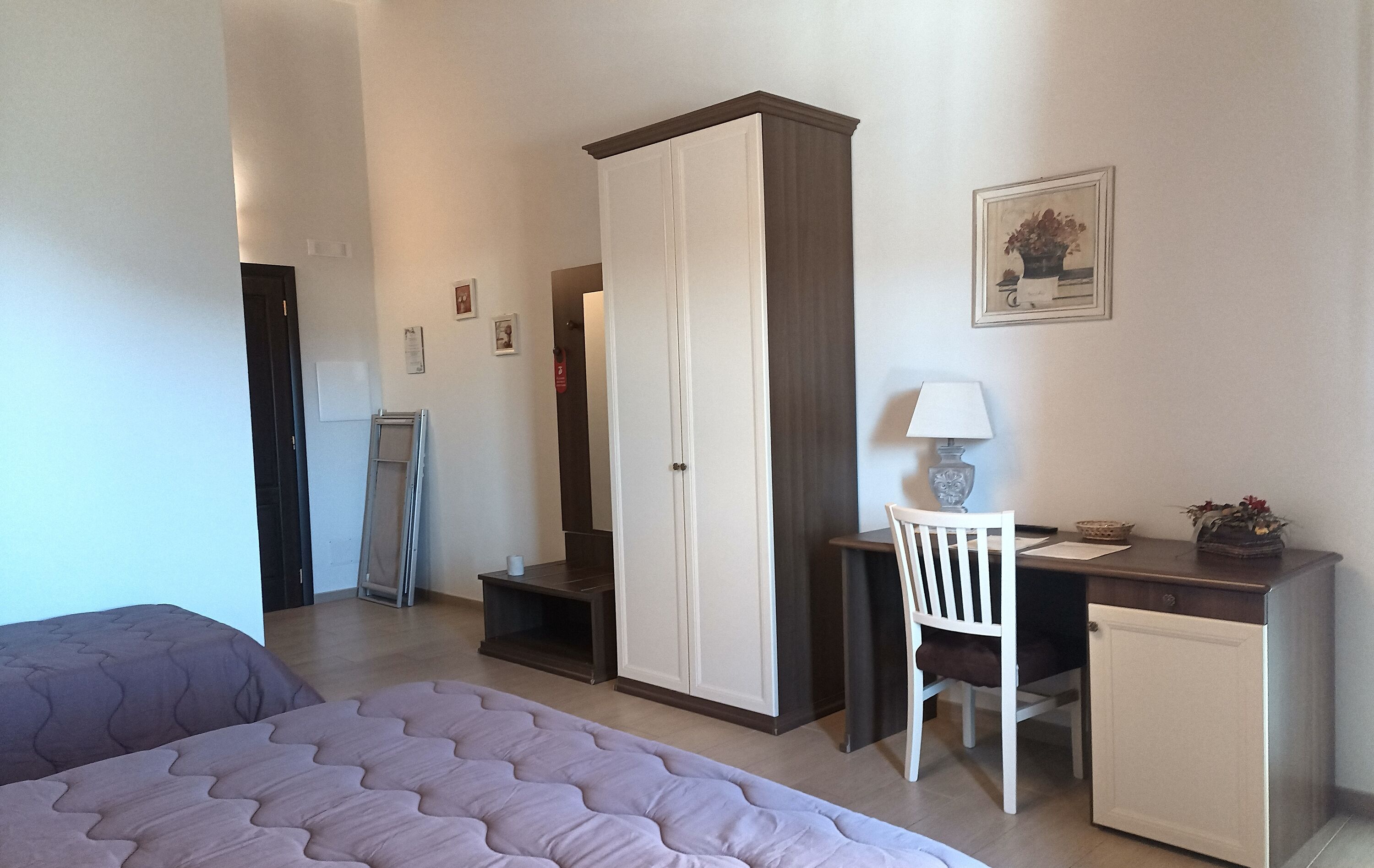 A bedroom with a bed, a desk, a chair, a wardrobe, and a small cabinet.