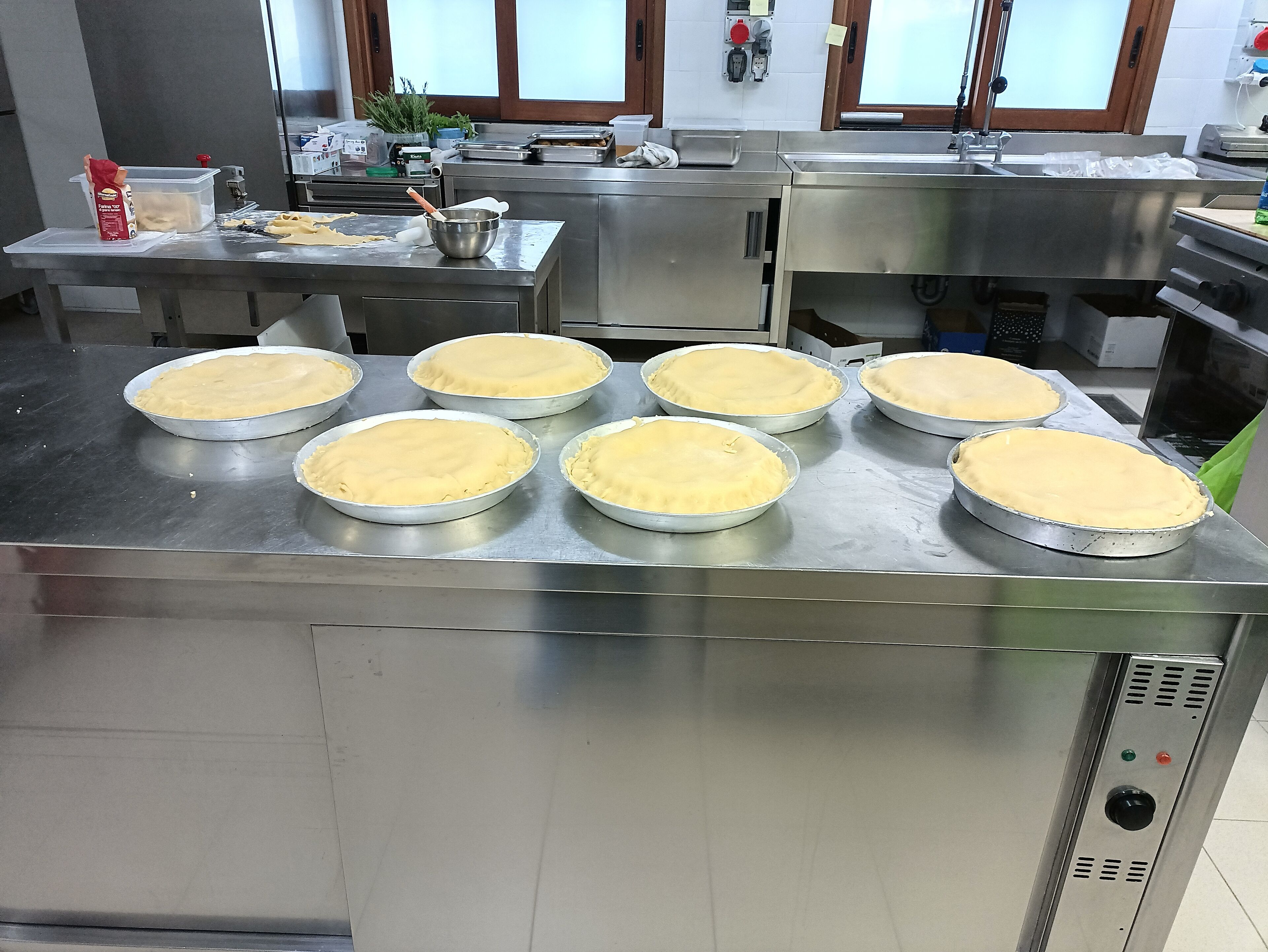 A commercial kitchen with multiple pie crusts lined up on a stainless steel counter.