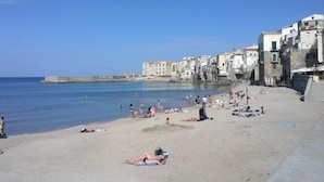 Une plage où l’on peut voir des gens se prélasser au soleil et nager, ainsi que des bâtiments dotés de balcons le long de la côte.