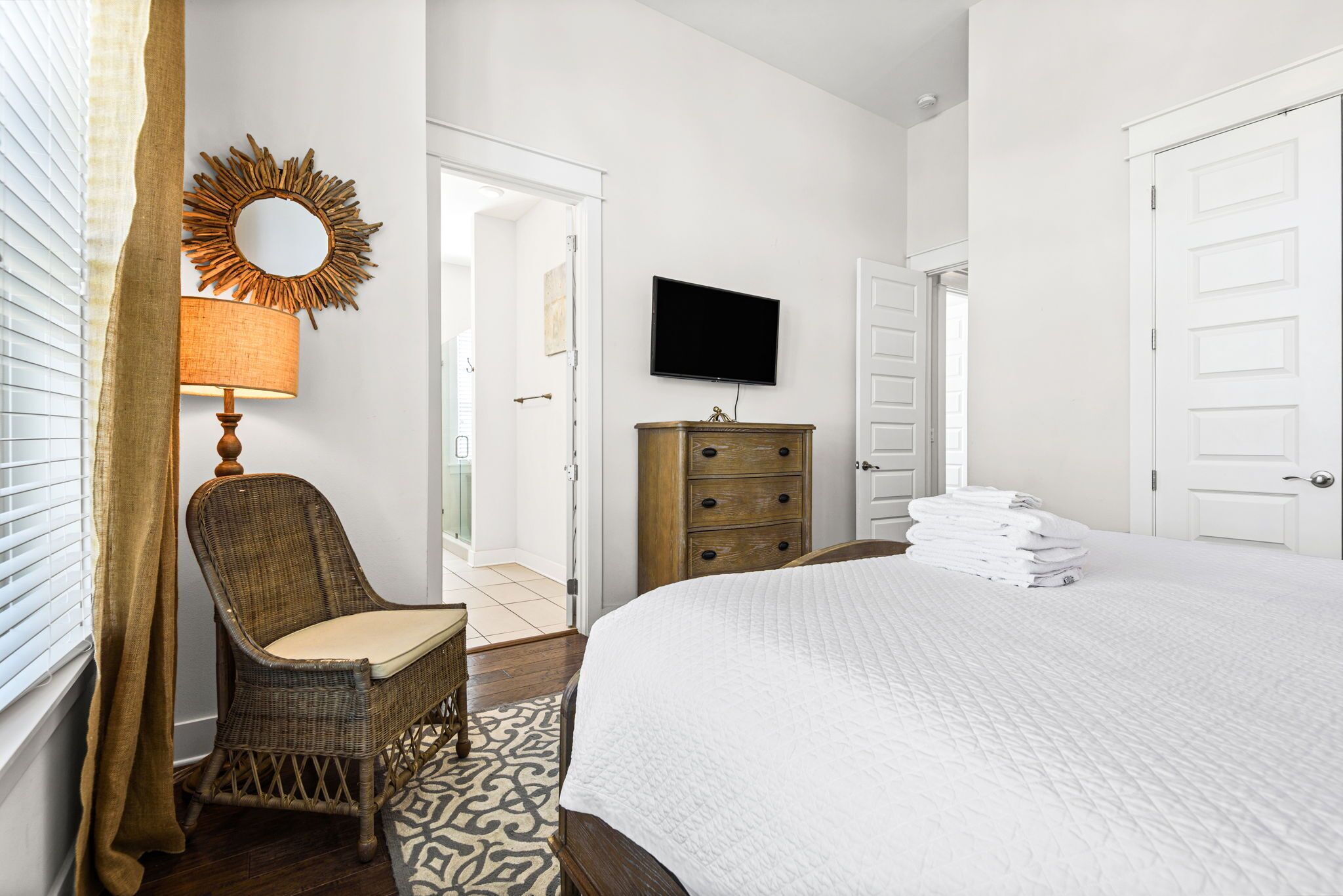 A hotel room with a bed, a television, a wooden dresser, and a wicker chair.