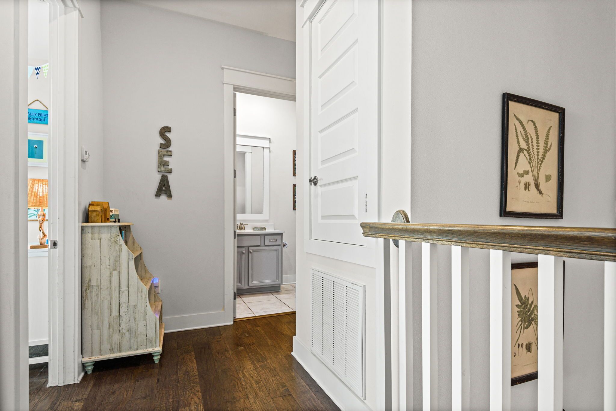 A hallway with a white door, a framed botanical print, and a wall-mounted sign.