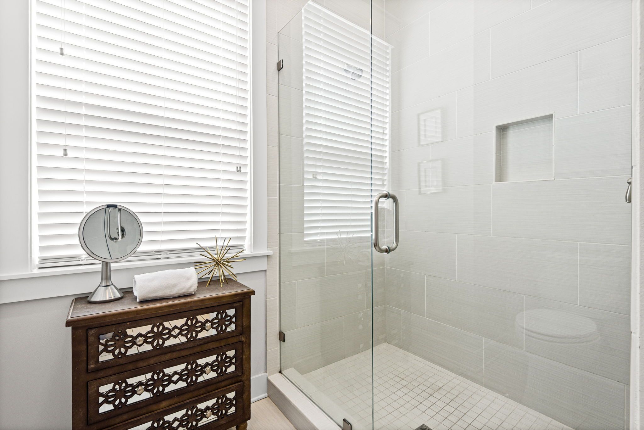 Une salle de bain avec une douche à parois de verre, un meuble-lavabo en bois avec un miroir et une fenêtre avec des stores.