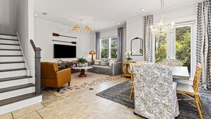 A modern living room with a staircase, a sofa, a dining table, and a TV. - Pet Friendly & A Minute From Prominence Pool, Sleeps 8 (Santa Rosa Beach)