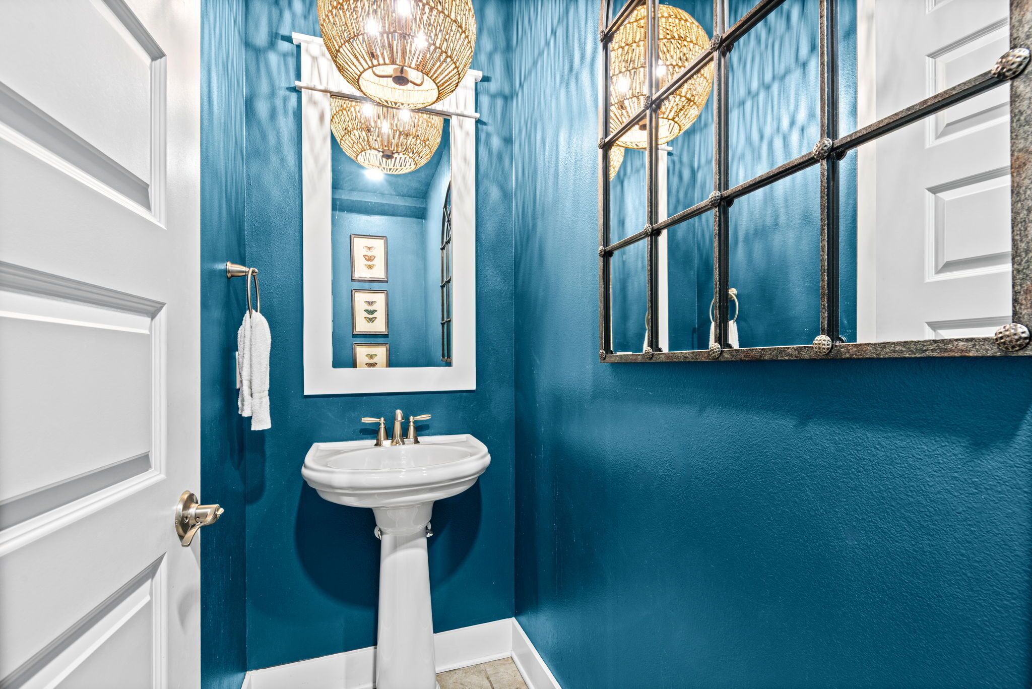 A bathroom with a white sink, blue walls, a mirror, and a chandelier.