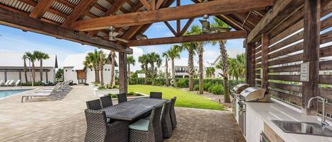 An outdoor patio with a wooden pergola, a pool, lounge chairs, and a grill area.