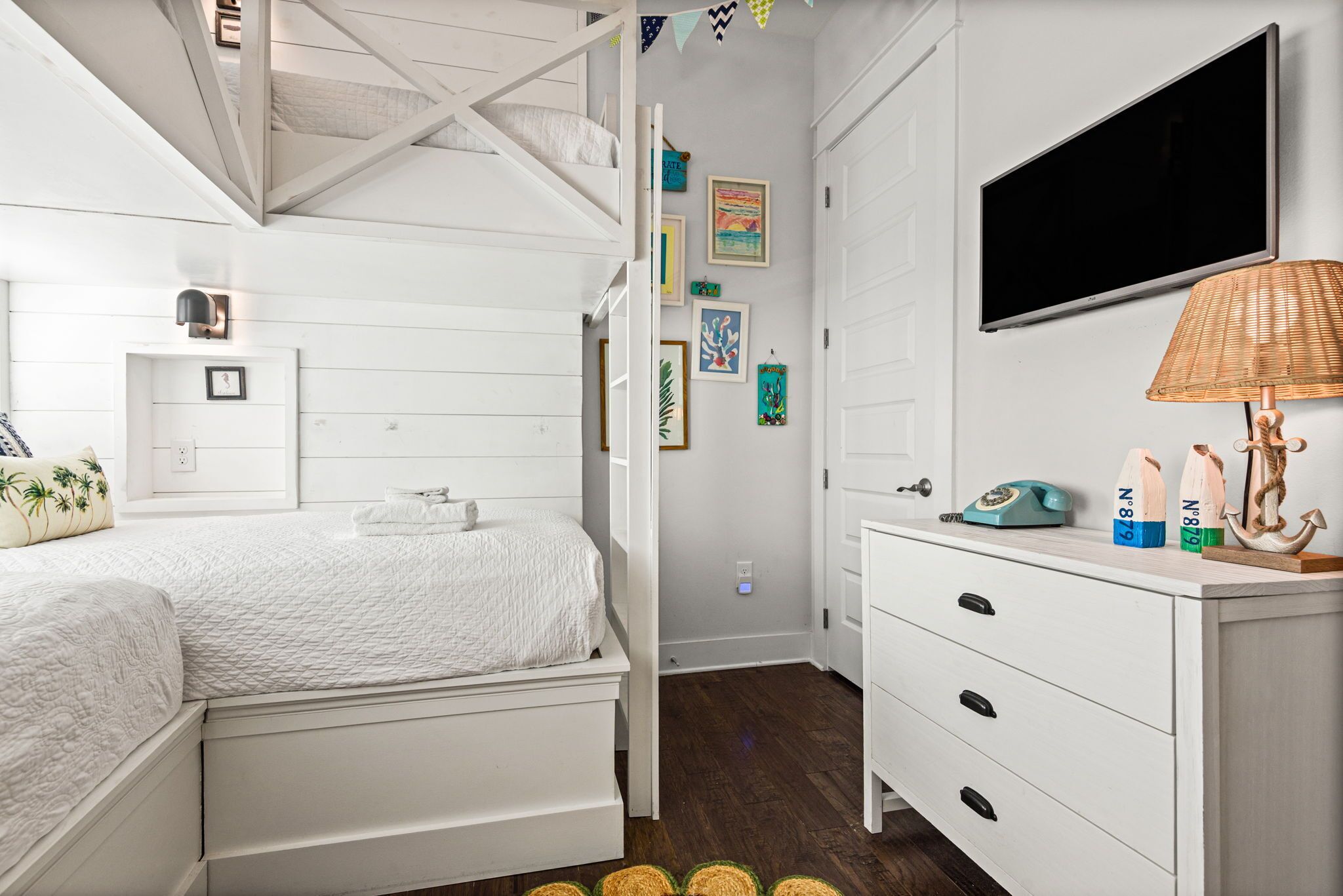 Une chambre avec un lit superposé, une table de chevet avec une lampe, une commode et des œuvres d’art accrochées au mur.
