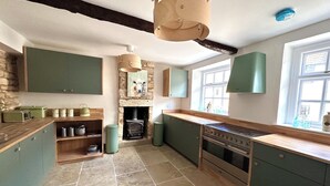 A kitchen with green cabinets, a stone fireplace, and a large window. - Honey stone and style year round (Winchcombe)