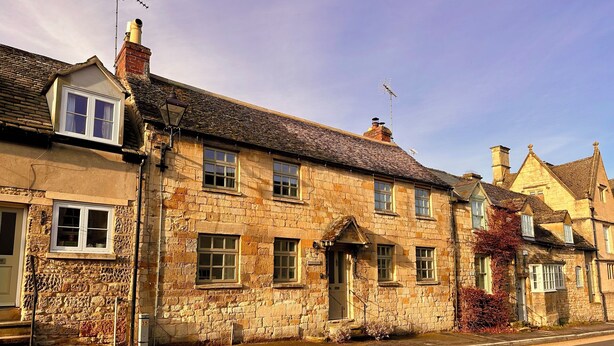 A traditional stone building with multiple windows and a chimney, located on a street with a sidewalk. - Honey stone and style year round (Winchcombe)