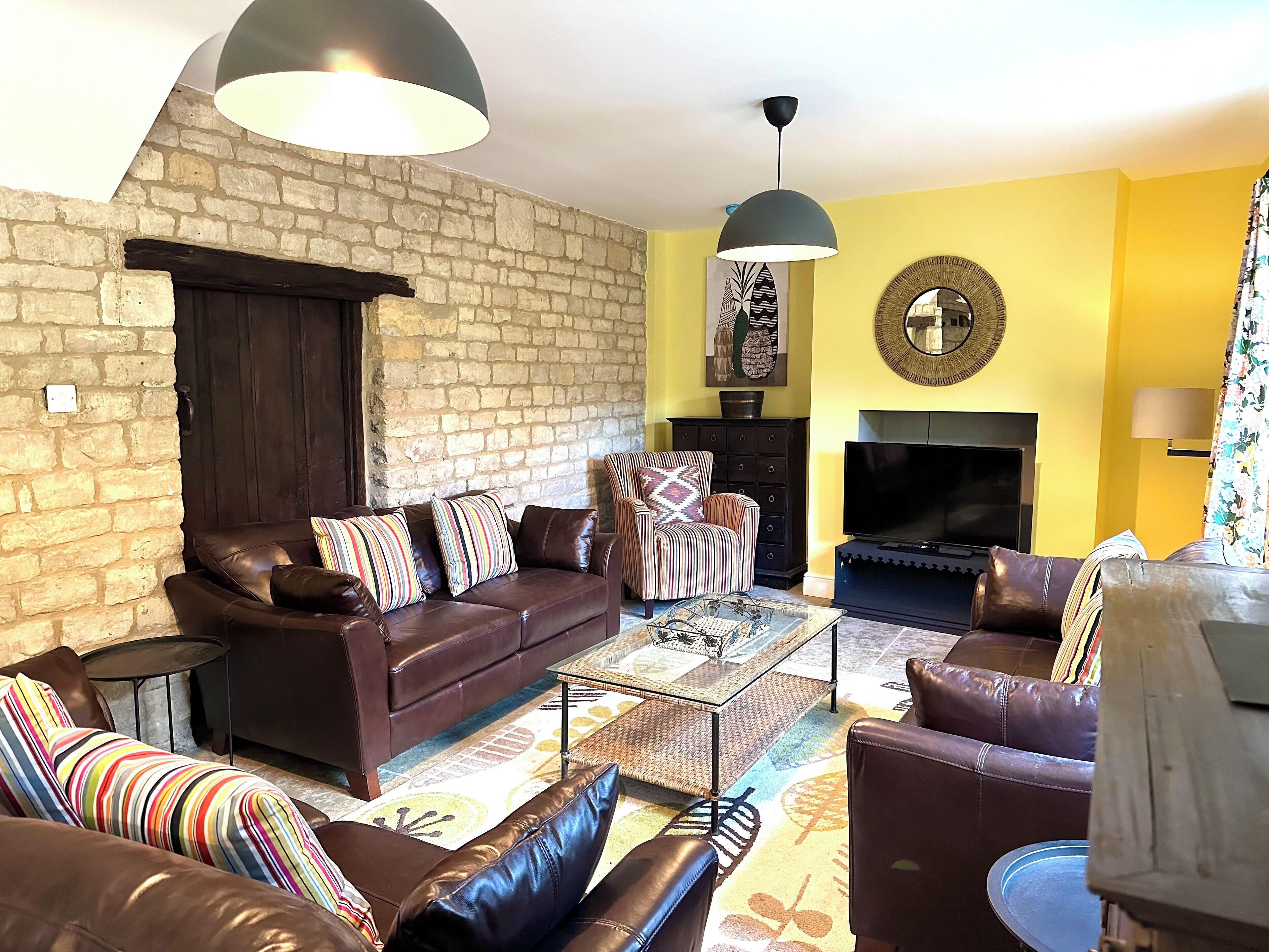 A living room with a brown leather sofa, striped pillows, a glass coffee table, a striped armchair, and a fireplace.