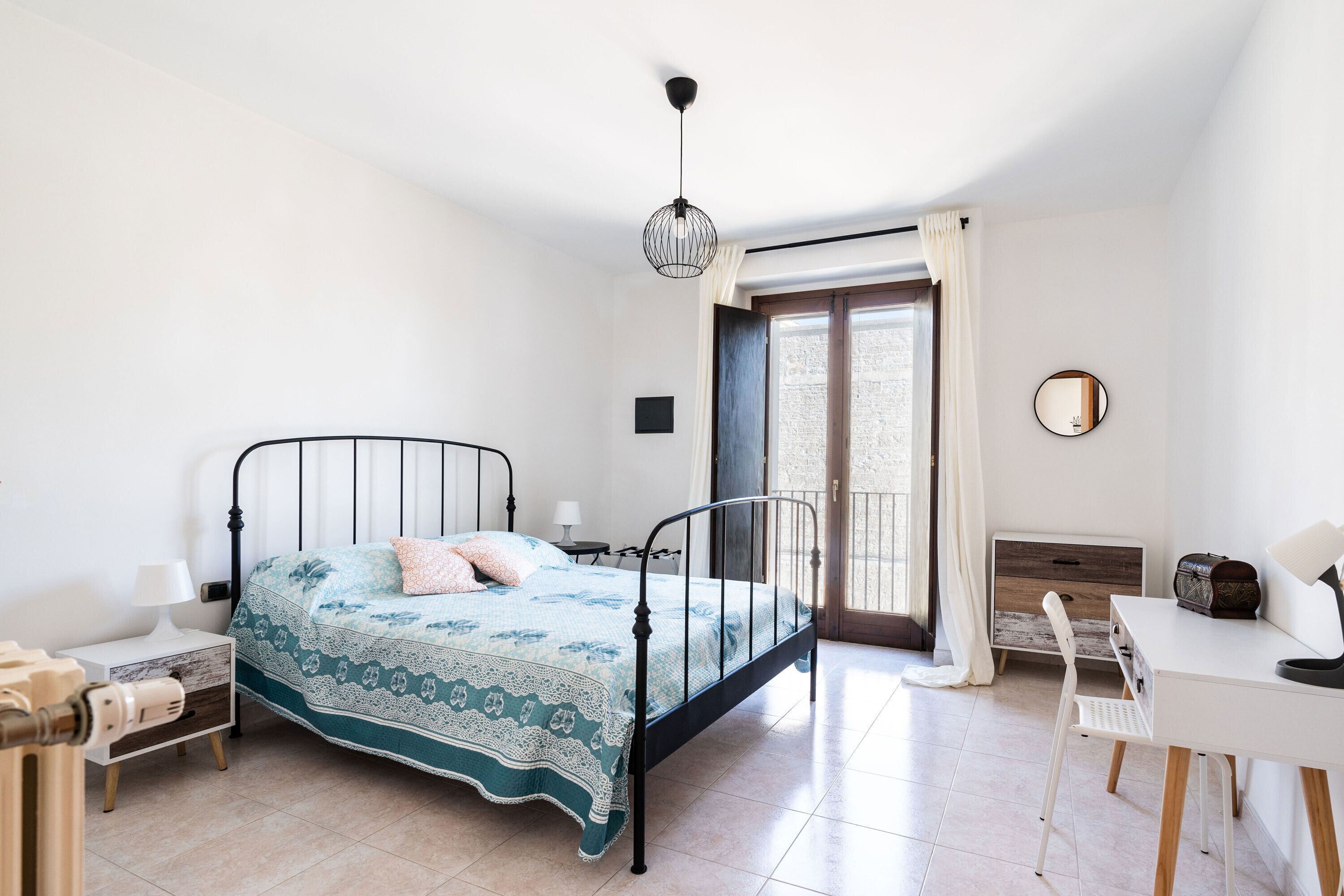 Una camera da letto con un letto, un comodino, una lampada, una sedia e una scrivania con la sua poltrona.
