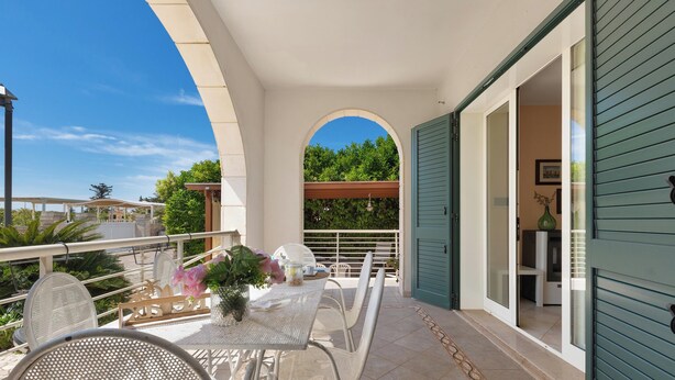 Un balcon avec une table et des chaises, un pot de fleurs et une vue sur la verdure.