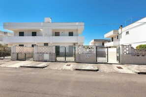 A modern two-story residential building with a gated entrance and a paved driveway.
