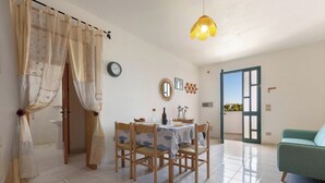 A dining area with a table set for four, wooden chairs, a hanging light fixture, and a green sofa in the background. - Casa di Tosca by BarbarHouse (Torre dell'Orso)