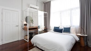 A modern hotel room with a large bed, a wardrobe, a round mirror, and a window with curtains.