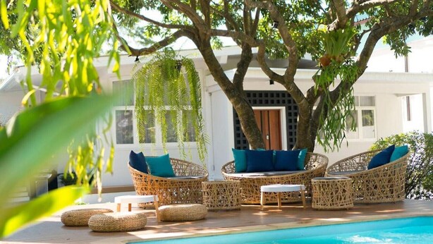 A poolside area with wicker furniture, a tree, and a building in the background.
