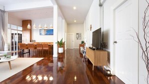 A modern living room with a dining area, wooden flooring, a TV on a wooden stand, and a large window.