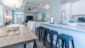 A modern kitchen with white cabinets, a wooden dining table, and black bar stools. - Pet Friendly + Private Pool; Amazing Fenced Backyard, 5 Min Walk to Beach! (Panama City Beach)