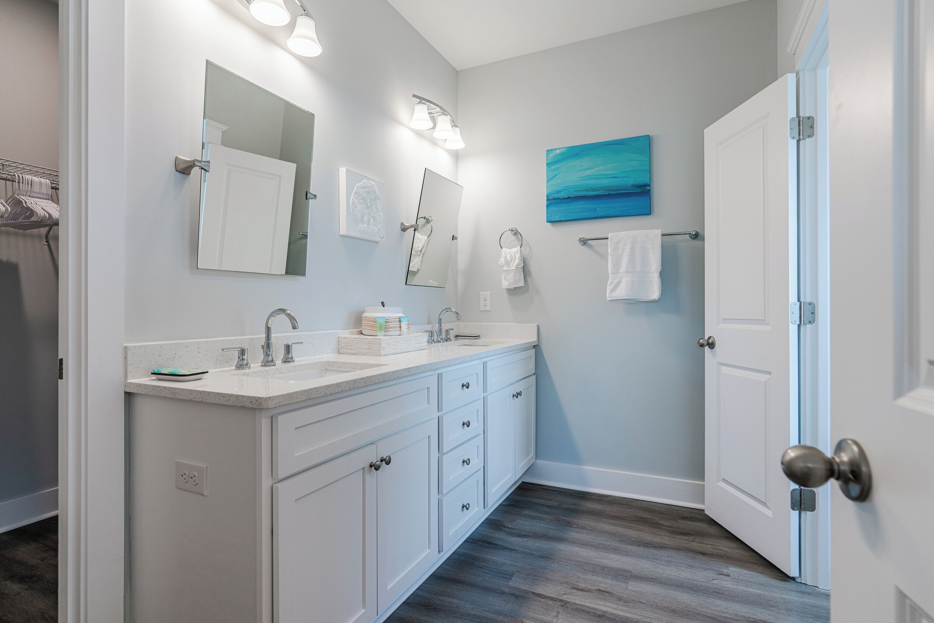 A bathroom with a white vanity, two sinks, a large mirror, and a painting on the wall.