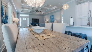 A modern kitchen with white cabinetry, a central island, and a dining area with a wooden table and chairs. - Pet Friendly + Private Pool; Amazing Fenced Backyard, 5 Min Walk to Beach! (Panama City Beach)