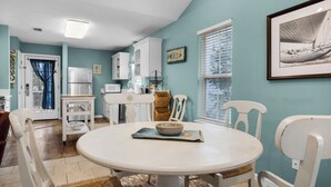A kitchen with white cabinets, a white refrigerator, a microwave, and a sink. There is a dining table with chairs and a bowl on the table. - Pet Friendly Beach Home; 2 Minutes to Beach & Eastern Lake (Santa Rosa Beach)