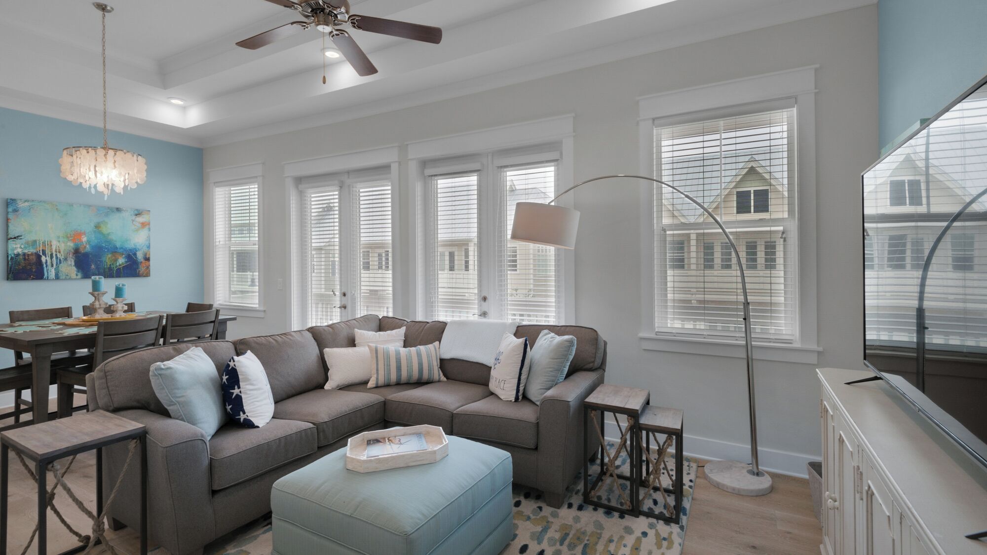 A modern living room with a sectional sofa, a dining table, and a chandelier.