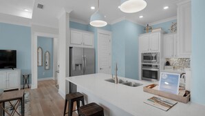 Une cuisine moderne avec des meubles blancs, des appareils en acier inoxydable et un îlot central doté d’un évier.