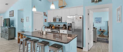 A modern kitchen with a central island, bar stools, a microwave, stove, refrigerator, and a sailboat decoration.