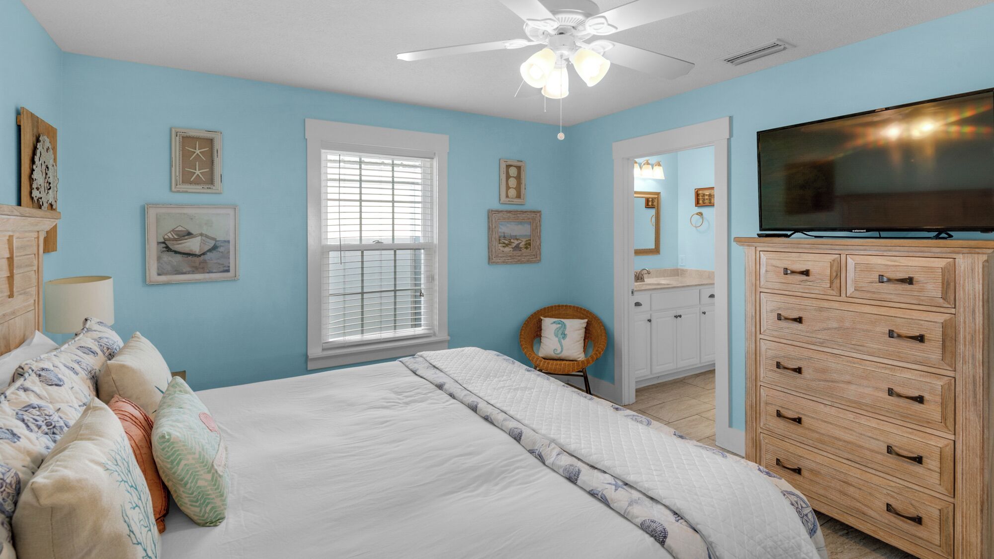 A bedroom with a bed, dresser, TV, and artwork on the walls.