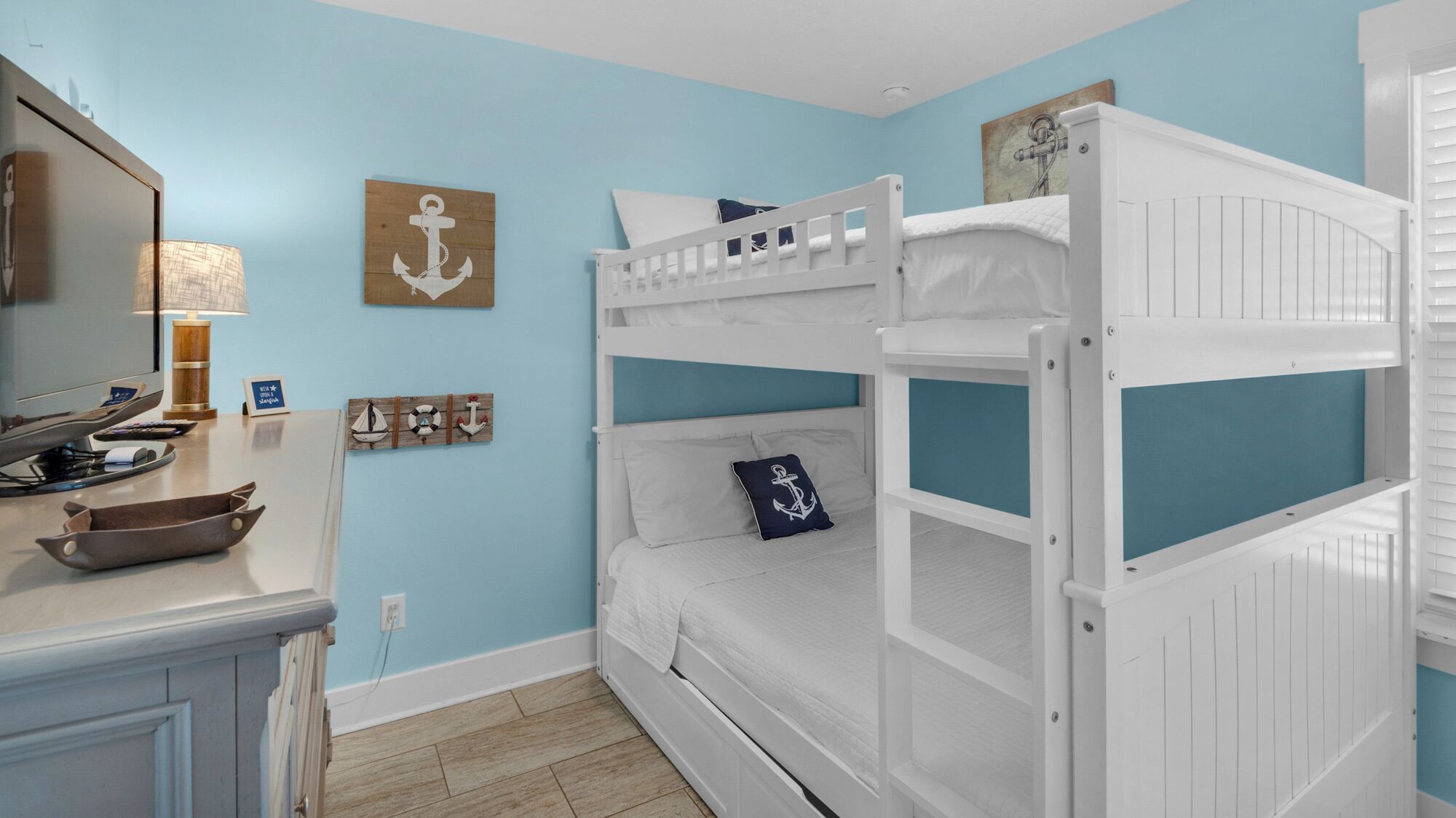 A bunk bed room with a wooden desk, a lamp, and nautical-themed decor.