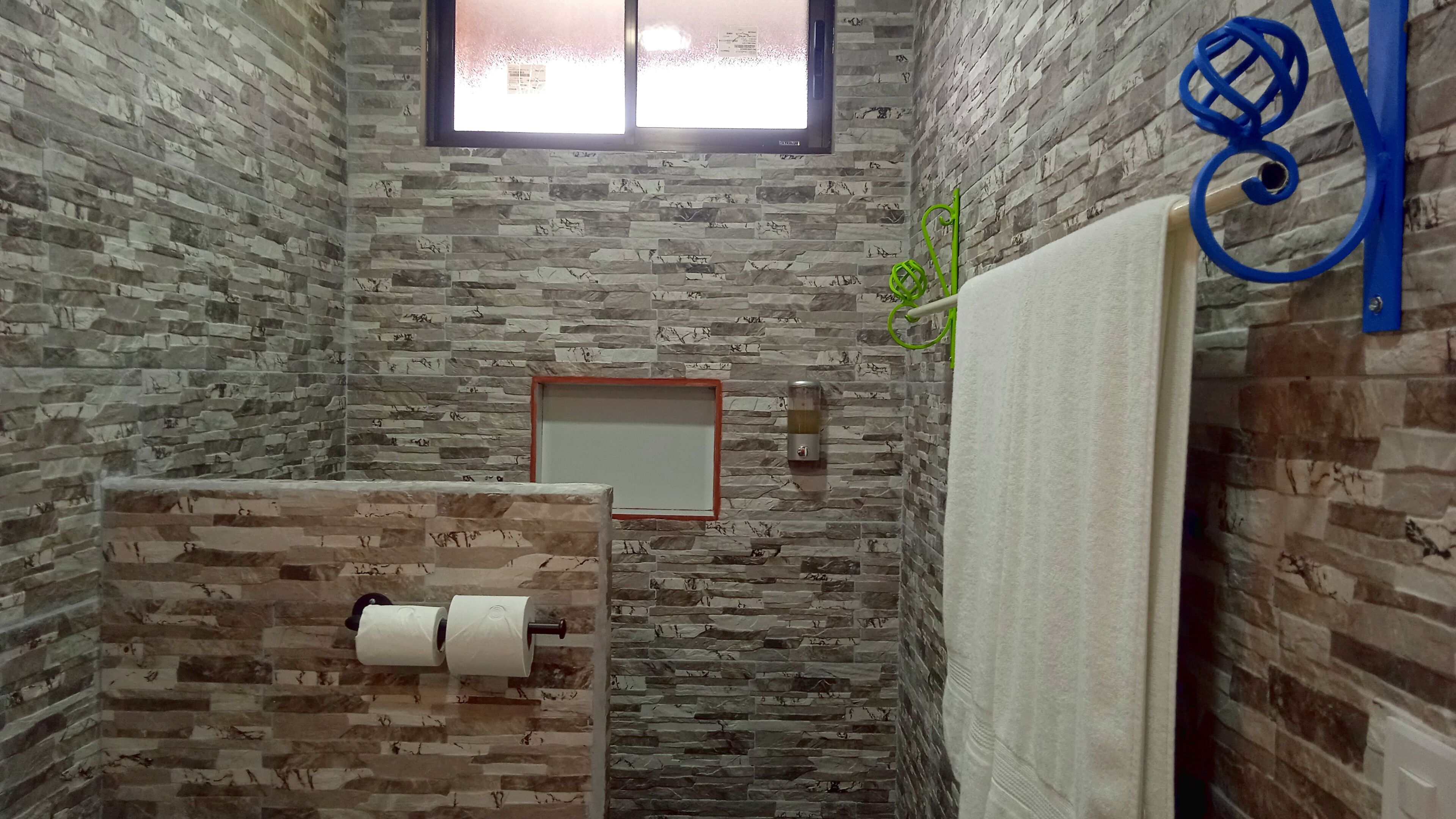 Une salle de bain avec un mur en pierre, une fenêtre, un porte-serviettes et un support à papier toilette.