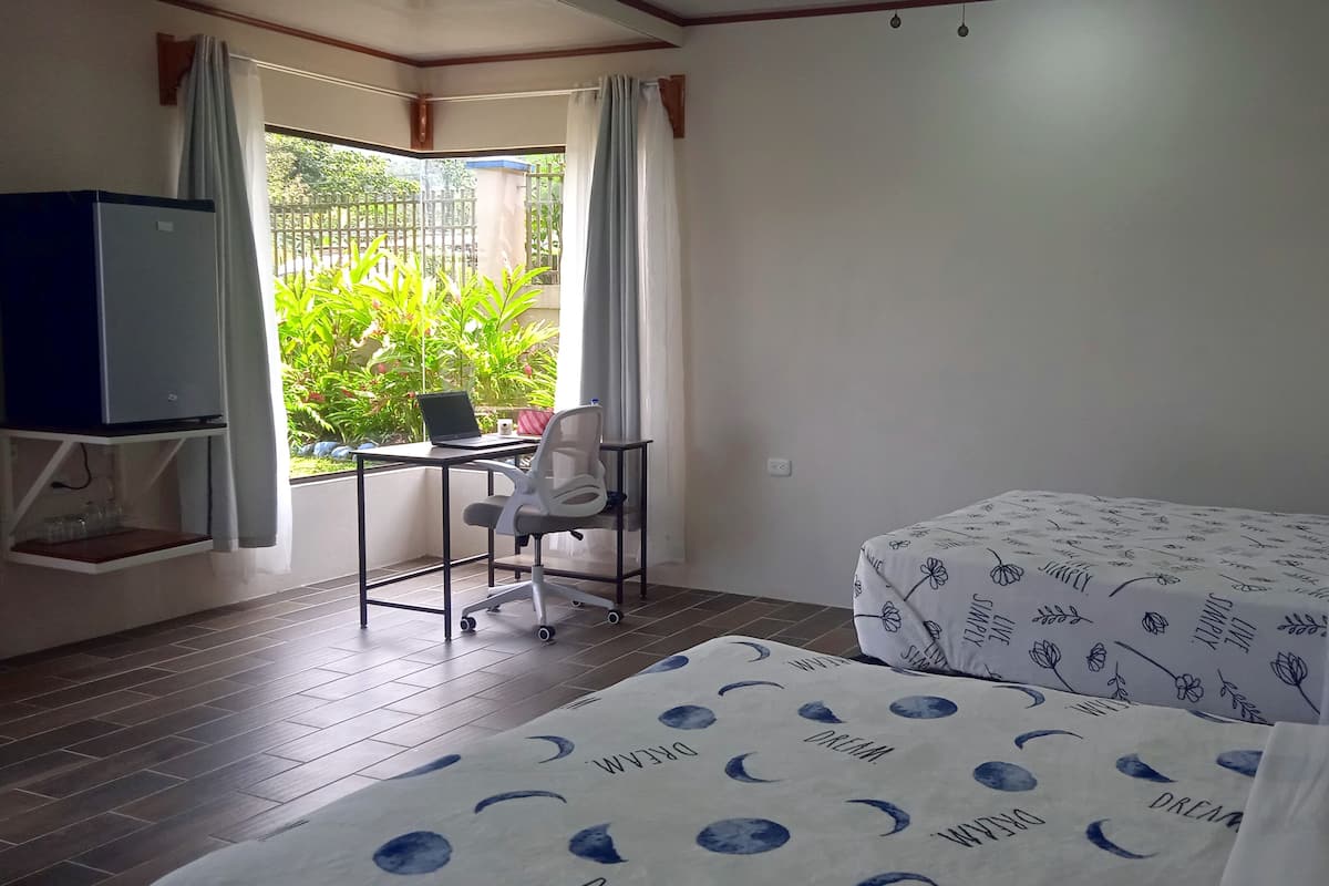 Une chambre avec un lit, un bureau avec un ordinateur portable, une chaise et un téléviseur posé sur un meuble.