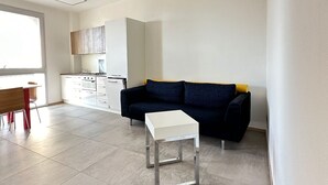 Un grand espace de vie comprenant un canapé, une petite table blanche et une cuisine à l’arrière-plan.