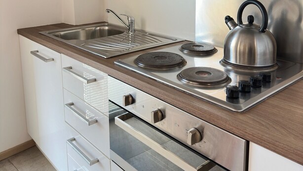 Une cuisine moderne dotée d’appareils électroménagers en acier inoxydable, de meubles de rangement en bois et d’une bouilloire sur la cuisinière.