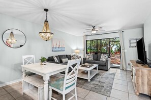 Un salon moderne comprenant un coin repas, un ventilateur de plafond et une grande fenêtre donnant sur un paysage verdoyant.