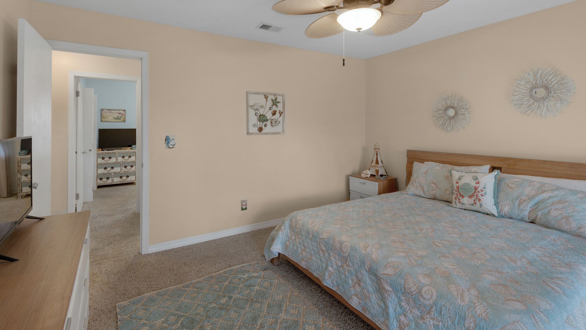 A bedroom with a bed, a nightstand, a ceiling fan, and a door leading to another room.