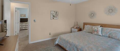 A bedroom with a bed, a nightstand, a ceiling fan, and a door leading to another room.