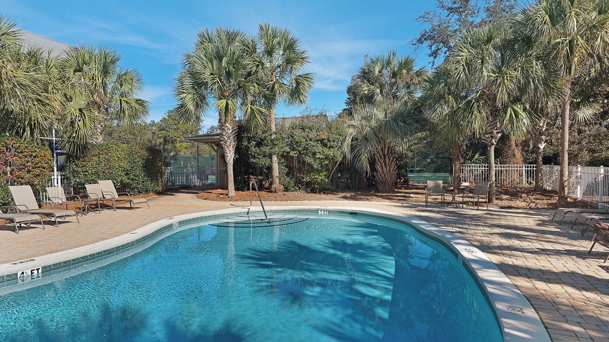 A swimming pool with lounge chairs and a covered seating area surrounded by palm trees.