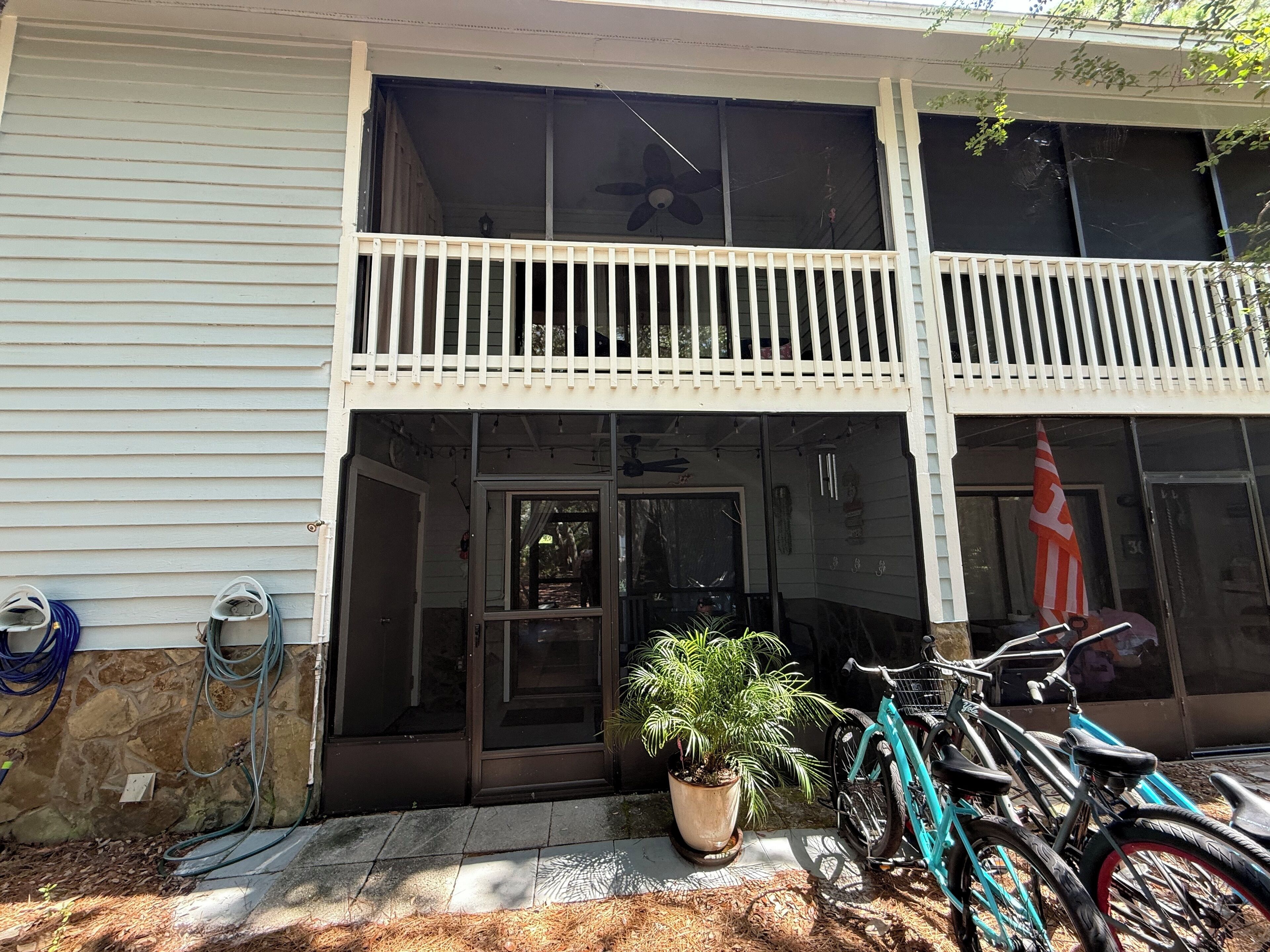 A two-story building with a balcony, a potted plant, and bicycles parked outside.