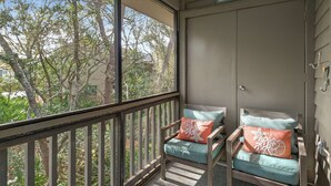 A balcony with two wooden chairs, each with a cushion and a decorative pillow.