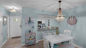 A kitchen with a white table, chairs, a hanging light fixture, and a clock on the wall.