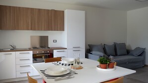 A modern kitchen with white cabinets, a wooden countertop, and a dining area with a white table set for two. - Spacious apartment in the heart of the Dolomites (Sospirolo)