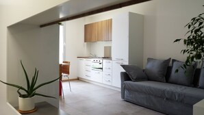 A modern kitchen with white cabinets, a built-in oven, and a grey sofa in a living area. - Spacious apartment in the heart of the Dolomites (Sospirolo)