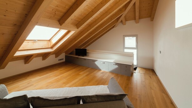 Een slaapkamer in loftstijl met houten balken, een dakraam, een inbouwkantoor en een bank.