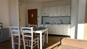 Una cocina compacta con armarios blancos, una mesa de comedor con sillas y suelo de madera.