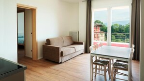 Una sala moderna con sofá, mesa de comedor y sillas. Se ve un balcón con barandilla y un edificio al fondo.